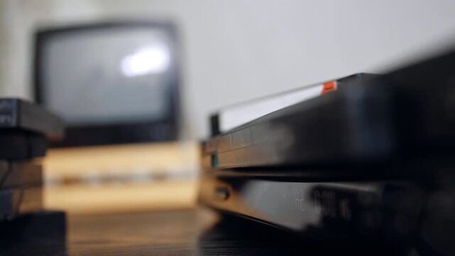 Inserting tape into old video player. A VHS cassette is guided into a vintage video recorder placed near an old TV set.