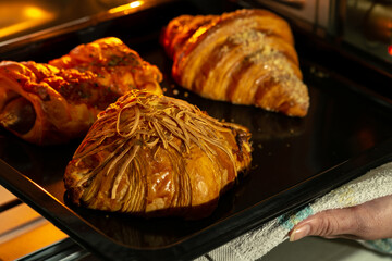 A close-up shows golden-brown pastries, including one topped with shredded cheese, on a black baking tray. A hand with a kitchen towel reaches for the tray.