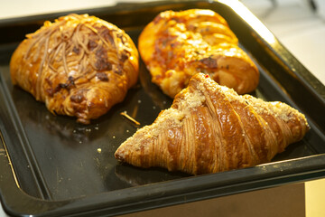 A high-angle close-up of three assorted golden-brown pastries, including a croissant and savory cheese-topped items, on a black baking tray.