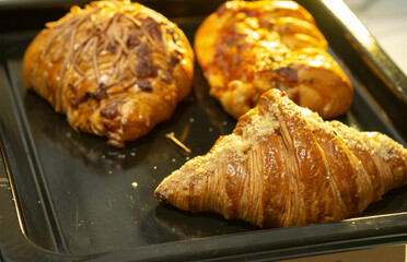 A high-angle close-up of three assorted golden-brown pastries, including a croissant and savory cheese-topped items, on a black baking tray.