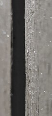Close-up of a textured wooden surface with a narrow gap. The wood is gray with visible grain and small particles of dust.