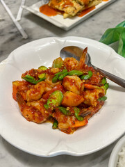 A high-angle view of Sambal Udang Petai, an Indonesian dish of prawns (udang) and stink beans (petai) stir-fried in a spicy red sambal chili sauce, served in a white bowl.