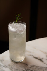 Tall, refreshing white cocktail with rosemary garnish on marble table