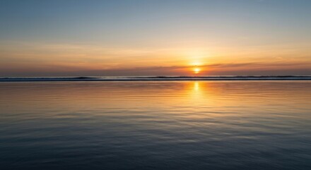 Naklejka premium Blurry sunset over a calm beach. Ocean water reflects golden hues of the setting sun. Soft colors, tranquil scene
