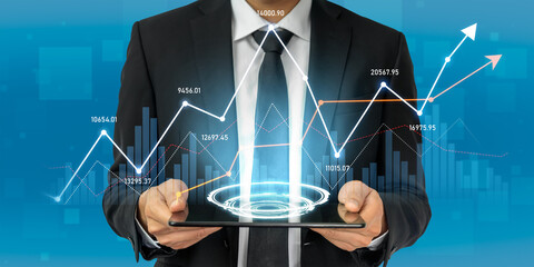 A businessman in a formal suit holds a tablet displaying digital financial charts and data, symbolizing growth, trends, and analysis in the corporate landscape. Scalp