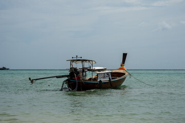 Fototapeta premium Traditional wooden Thai longtail boat anchored near the shore in calm turquoise water with the unique long propeller shaft clearly visible against a hazy horizon