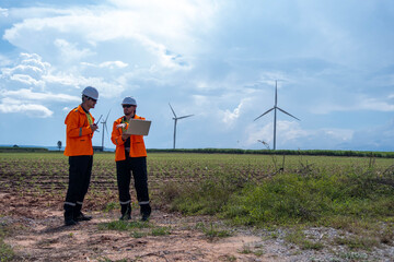 Engineers conduct field inspection near wind turbines under a cloudy sky in rural landscape