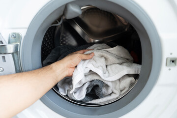 Close-up of a hand loading dirty clothes into a modern washing machine. Laundry day concept and household chores