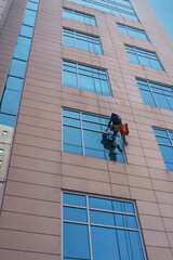 Window Cleaning On Modern Beige Facade By Rope-Access Worker Suspended From Height