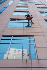 Rappelling Construction Worker Suspended on Rope Against Modern Glass Facade
