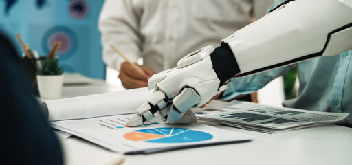 A robotic hand interacts with business reports and charts in a modern office, highlighting technology's role in teamwork and project analysis for enhanced productivity.Noogenesis