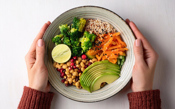 manos sostienen un plato de comida vegana, sobre fondo blanco, vista superior