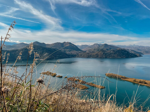 Grassy foreground overlooking tranquil mountain lake soft marsh patches, slender reeds, mirrored sky, layered ridgelines, - Powered by Adobe