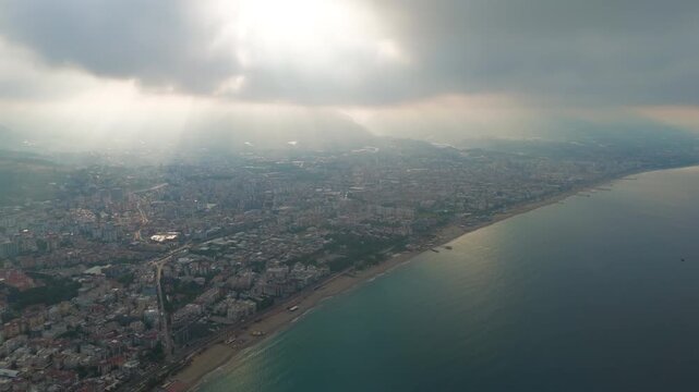 Alanya, Turkey. Aerial view of Oba Beach and Tosmur Beach with city, cloud-covered mountain slopes and sun rays over low sea clouds in summer.. Aerial View