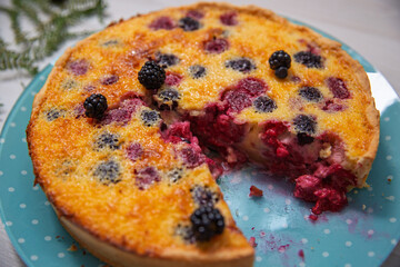 Homemade berry tart with blackberries and raspberries. One slice is removed, showing the juicy berry filling and golden crust. Close-up rustic dessert in natural light.