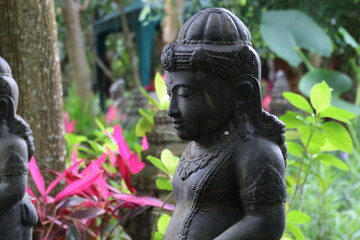 Obraz premium Stone statue stands peacefully among vibrant tropical plants in a lush garden, creating a serene and spiritual atmosphere.
