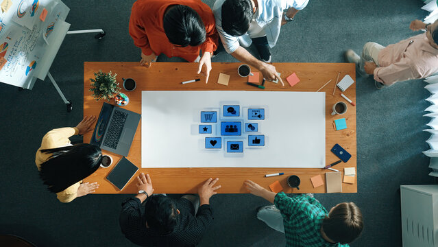 A diverse group of professionals collaborates on innovative ideas during a team meeting at a stylish workspace, surrounded by technology and creative materials. Trope - Powered by Adobe