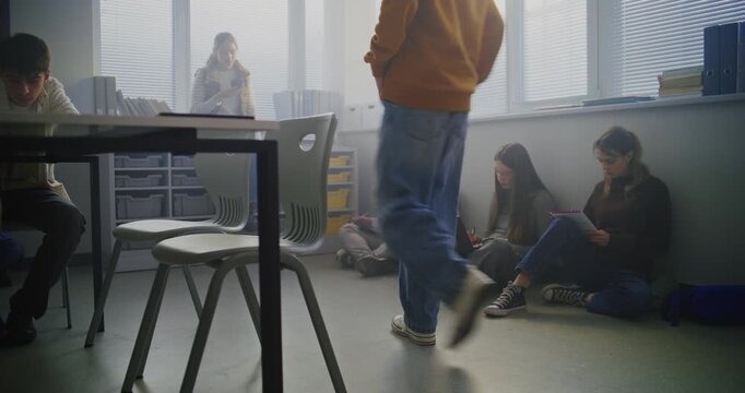 Group of Teenagers Sitting Comfortably on Classroom Floor, Writing in Notebooks and Discussing Ideas While Sharing Laptop. Concept Flexible Learning, Student Collaboration, and Creative Communication.
