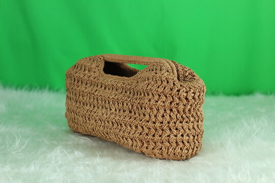 Crocheted cream bag on a white fluffy blanket in front of a green background.
