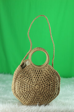 Crocheted cream bag on a white fluffy blanket in front of a green background.