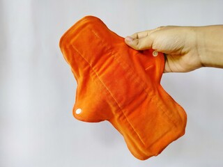 hand holding orange reusable menstrual cloth pad on white background 