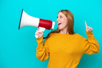 Young redhead woman isolated on blue background shouting through a megaphone to announce something...