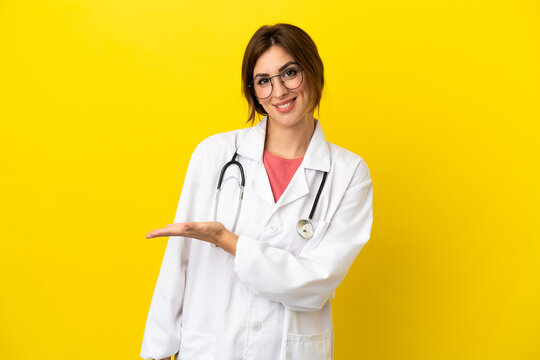 Doctor woman isolated on yellow background presenting an idea while looking smiling towards