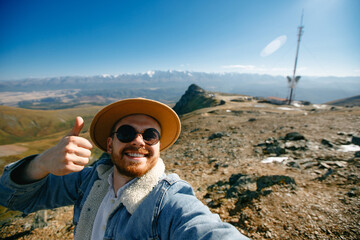 Young caucasian male taking selfie on Altay mountain peak Aktash repeater with thumbs up gesture