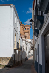 A charming street in Laujar de Andarax, Almeria, Spain, with whitewashed buildings and balconies. In the background, the Parish Church of the Incarnation rises with its brickwork and iconic bell tower