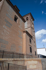 The bell tower of the Church of the Incarnation in Laujar de Andarax, Almeria, Spain, rises gracefully with brick walls, arched windows, and visible bells, set against a vivid blue sky