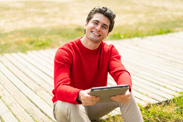 Obraz premium Young handsome man holding a tablet at outdoors with happy expression