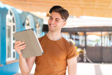Young handsome man holding a tablet at outdoors with happy expression