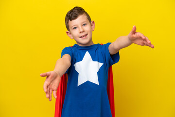 Little caucasian boy isolated on yellow background in superhero costume and doing coming gesture