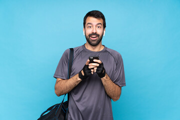 Young sport man with beard over isolated blue background surprised and sending a message