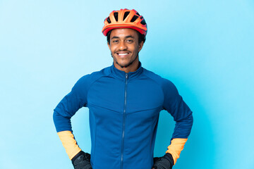 Young cyclist man with braids over isolated background posing with arms at hip and smiling