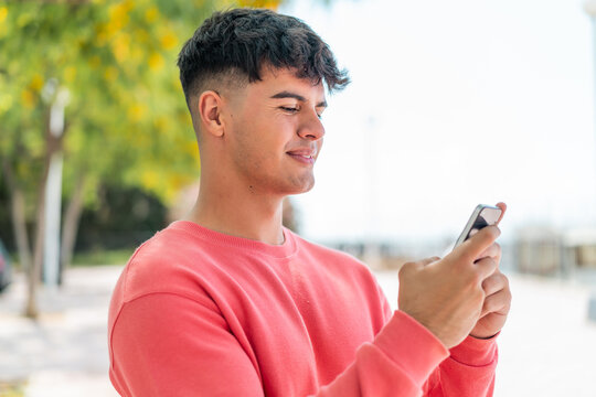 Young hispanic man at outdoors sending a message or email with the mobile