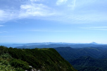 Mountain ridges and distant coastline under wide blue summer sky