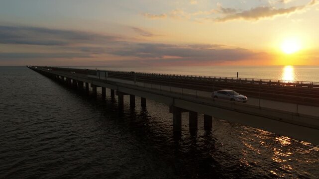 A slow-motion drone shot tracking along the west side of the Lake Pontchartrain Causeway as the sun sets, capturing warm golden-hour light and the long bridge stretching into the distance.