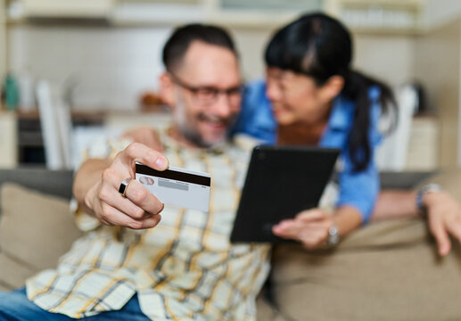 Portrait of a lovely young couple using a tablet computer and online shopping holding credit card together and having fun sitting on sofa at home