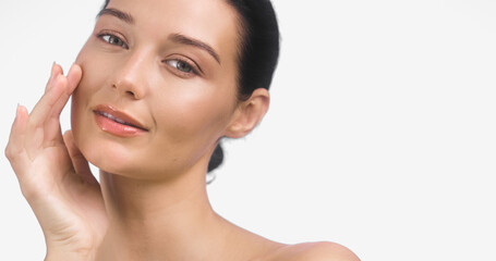 Young Woman Touching Face with Radiant Skin and Glossy Lips on White Background