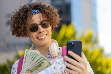 Happy rich Caucasian man counting holding money dollar cash, use smartphone calculator app, plans to order gifts and food delivery online, booking hotel room. Guy tourist in town city street, outdoors