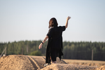 Young woman with dark hair wearing sunglasses poses confidently on sandy hill against clear blue...