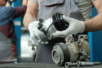 Fototapeta premium Car repair.Air conditioning system. Two car mechanics are preparing to replace a faulty air conditioner compressor and install a new compressor.