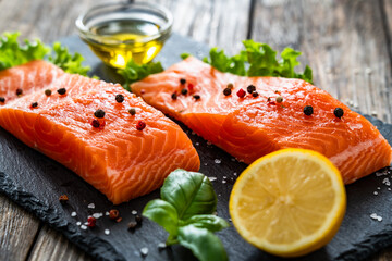 Fresh raw salmon steaks on black stony board on wooden background