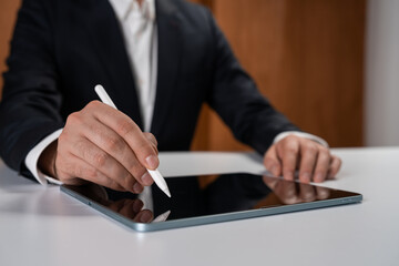Businessman using digital stylus on tablet device at desk in modern office environment, focusing on innovation and technology concept in business.