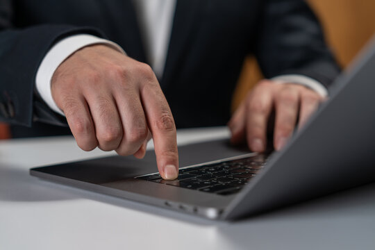 Businessman touching laptop keyboard with finger in office setting, highlighting technology interaction and professional gadget usage concept.