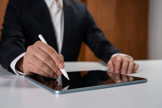 Businessman using digital stylus on tablet device at desk in modern office environment, focusing on innovation and technology concept in business.