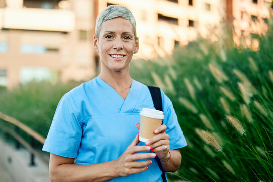 Nurse in scrubs enjoying coffee outside a modern medical facility during a sunny day