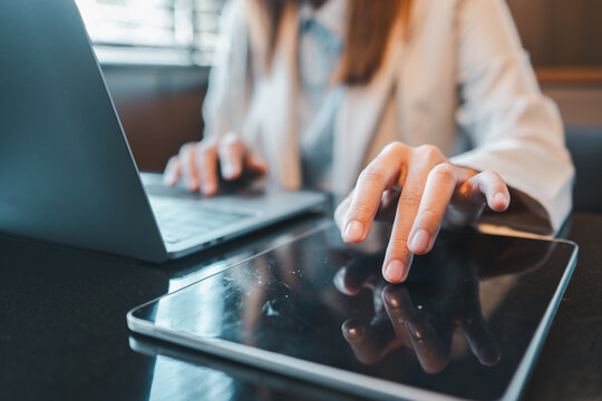 Close-up of a woman working on a laptop and tablet, showcasing multitasking in a modern office setting.