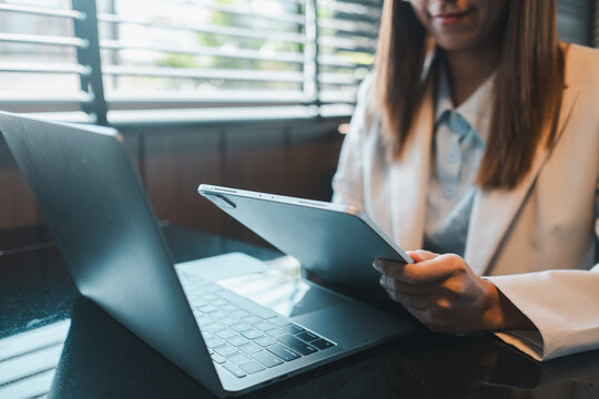 Professional woman multitasking with laptop and tablet in a contemporary office setting, illuminated by natural light.